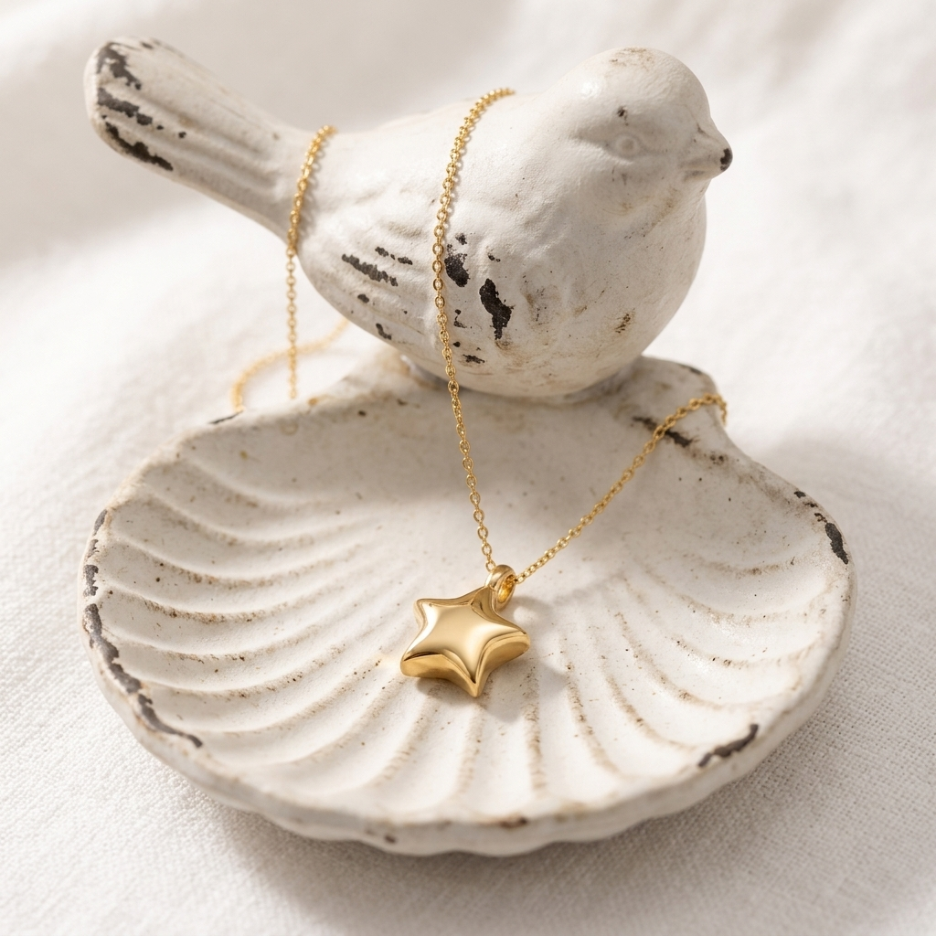 Gold Little Star Pendant Necklace draped over a white vintage bird figurine on a scalloped shell trinket dish, star charm resting in the dish.