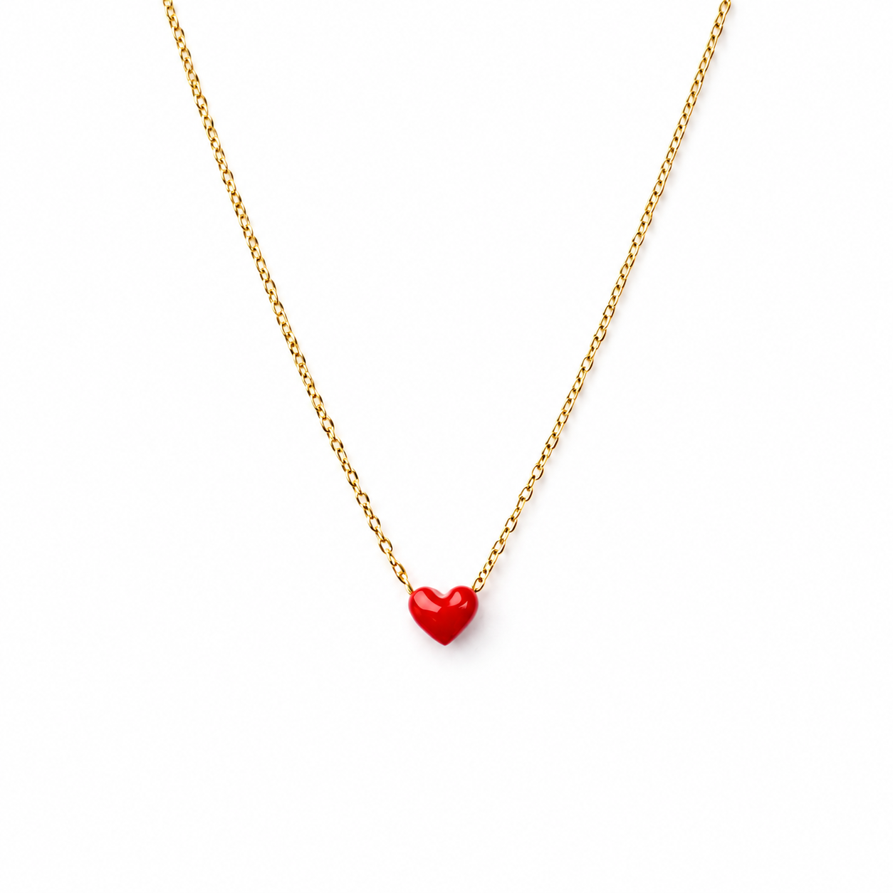 A delicate gold chain necklace featuring a small, glossy red heart-shaped pendant, displayed against a clean white background.