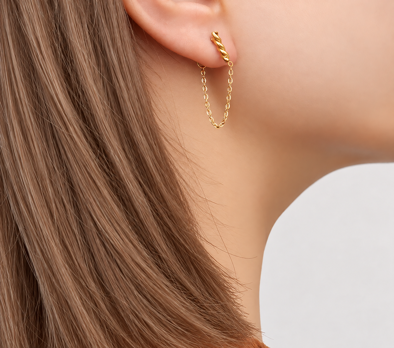 Model wearing Eternal Knot gold twisted stud earring with chain draping under the earlobe