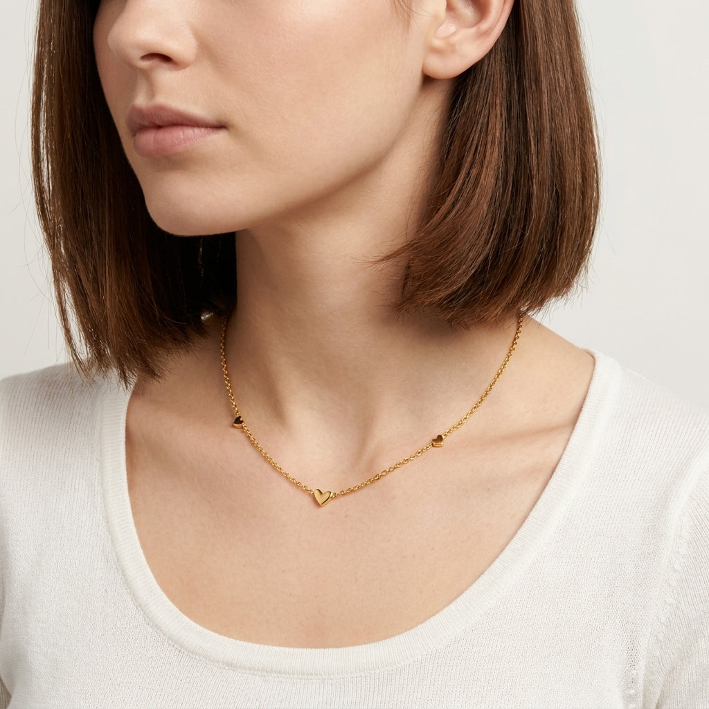 Model wearing the Heartline Necklace, a dainty gold heart necklace resting at the collarbone with a white top