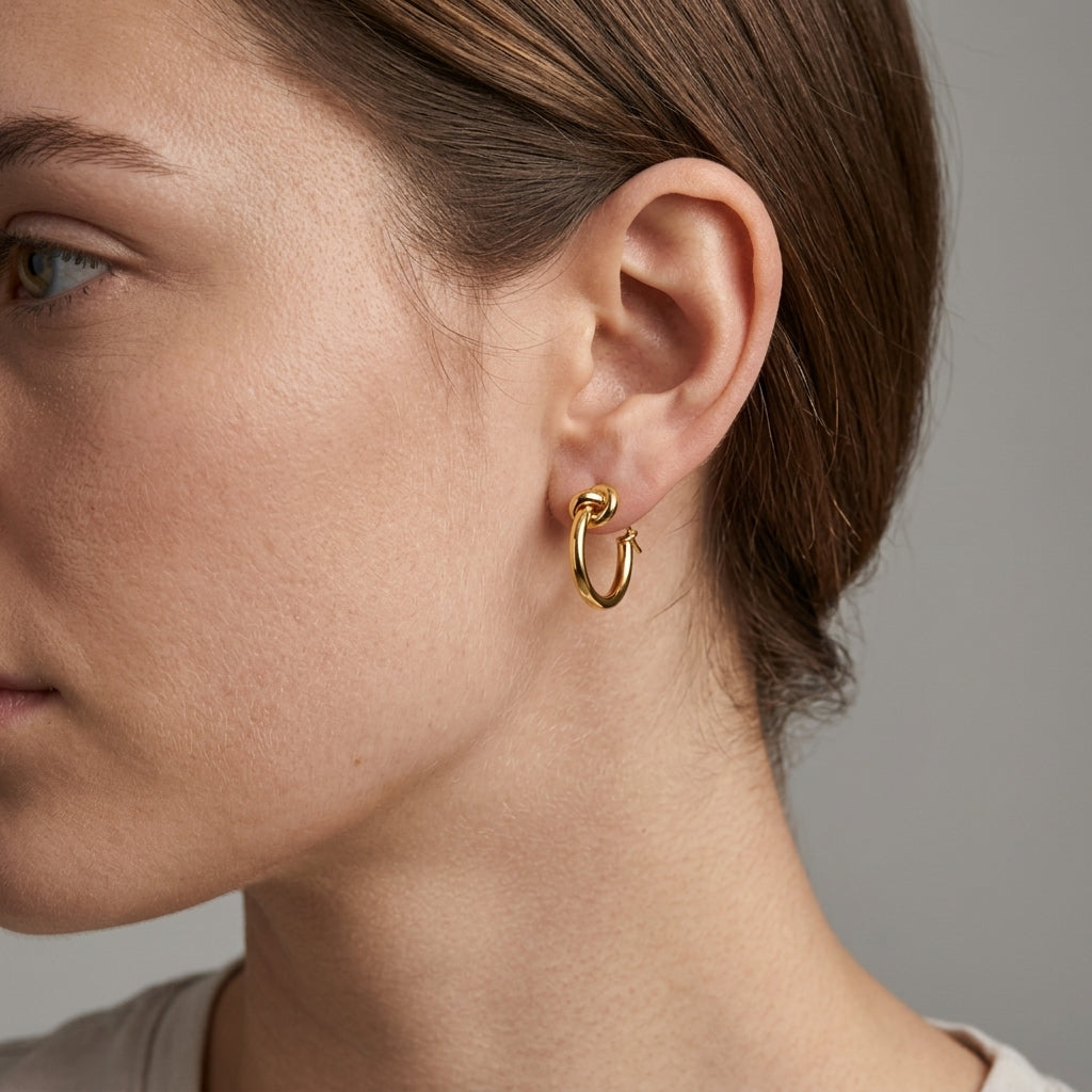 Close-up of a woman wearing a gold knot hoop earring, showing its petite size on the earlobe