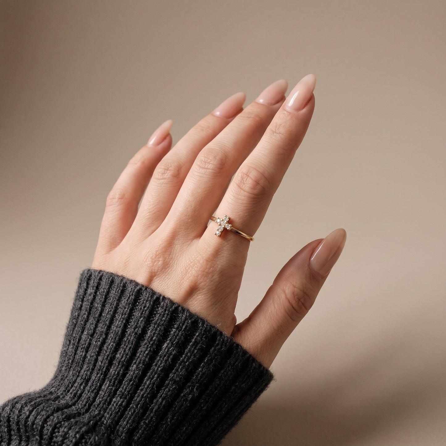Woman's hand wearing a dainty gold cross ring with clear stones on the middle finger