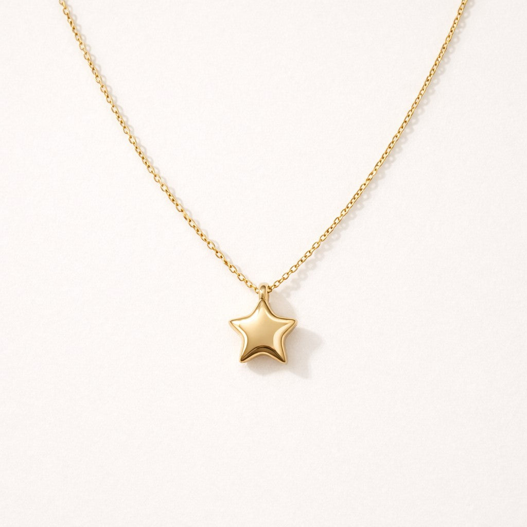Gold Little Star Pendant Necklace with a polished puffy star charm on a dainty cable chain, laid flat on a cream background.