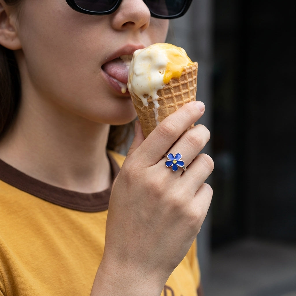 A close-up lifestyle shot of a person wearing a blue flower ring while eating an ice cream cone.