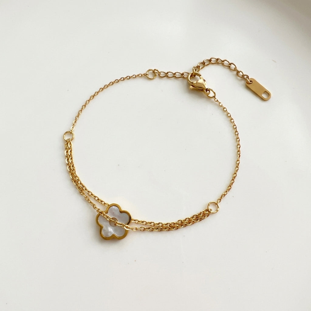 A delicate gold chain bracelet featuring a small four-leaf clover charm with a white inlay, displayed on a clean white background.